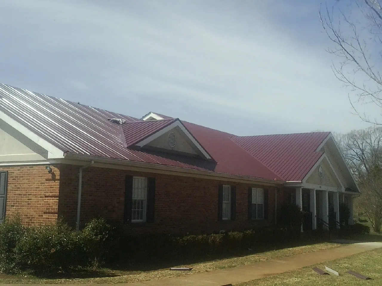 Red metal roof with gabled entries on a long brick building, from a Hail Damage Roof Repair job in Freeport