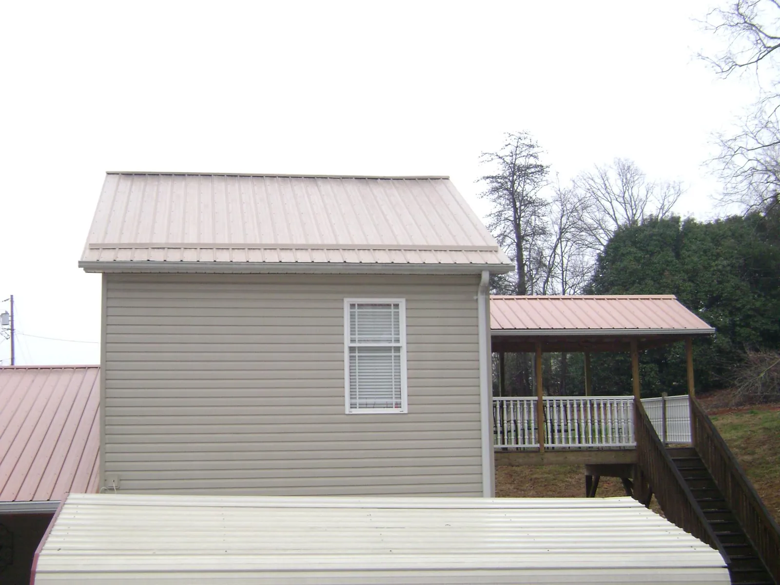 Tan metal roofs on a two story addition and attached porch, from a Roof Replacement job in Freeport